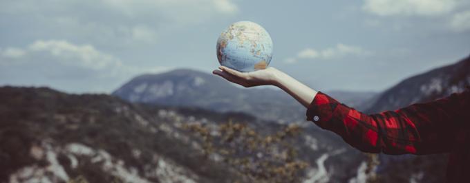 Person in a flannel shirt holding out their arm while holding a globe.